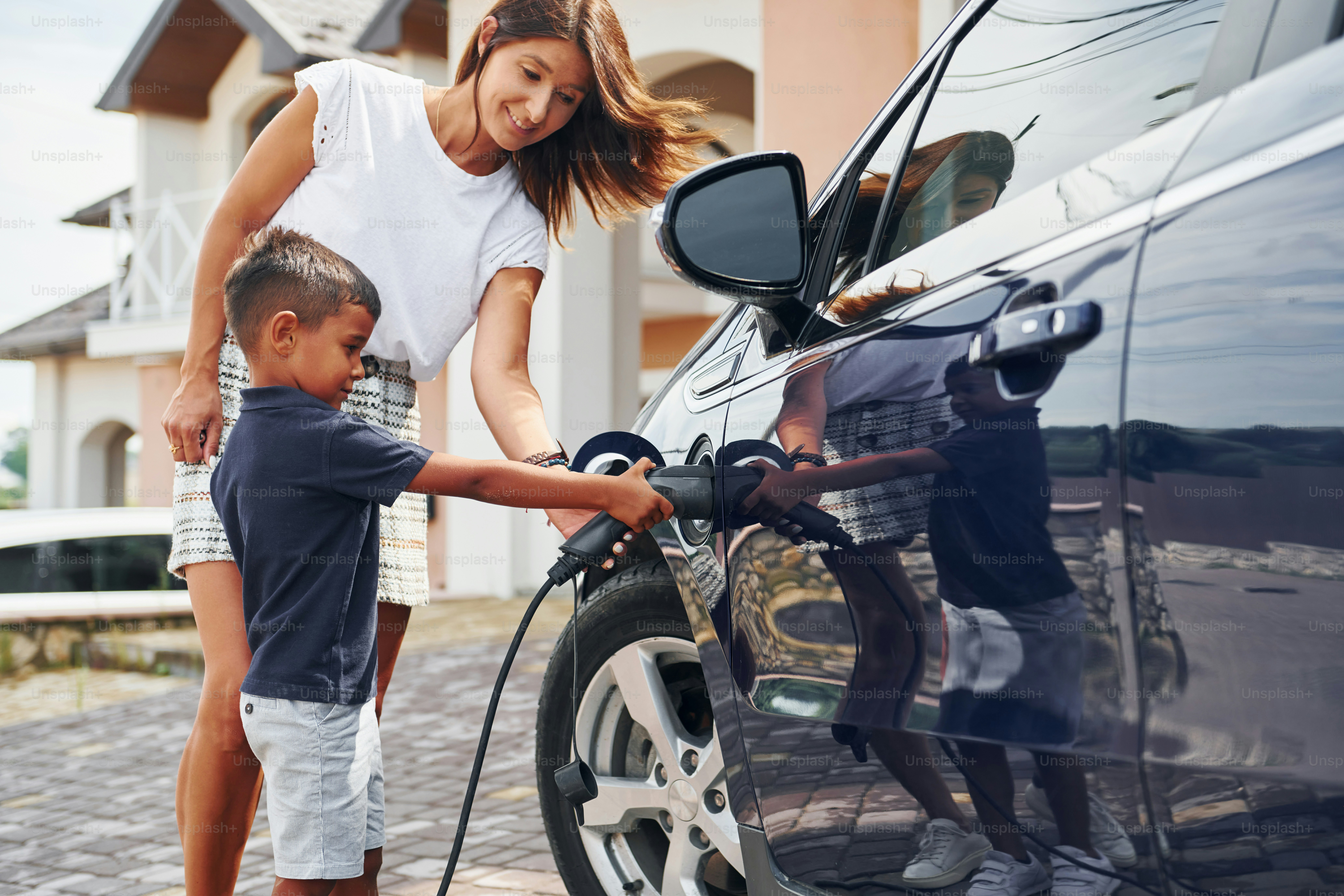 Charging the car. Woman with little boy near the the modern automobile at daytime.