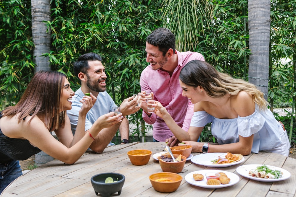 Group of Young latin Friends Meeting For beer, michelada Drinks And mexican Food Making A Toast In Restaurant terrace in Mexico Latin America