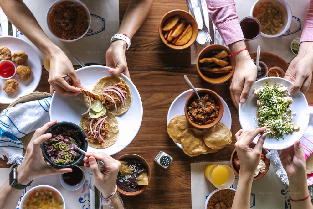 メキシコのタコスや伝統的な食べ物、スナック、テーブル、上面図の人々の手を食べるラテン系の友達のグループ。メキシコ料理ラテンアメリカ