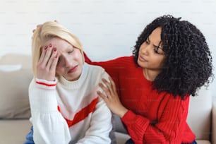 Friend trying to calm down her friend. Woman crying. Young lady sharing her problem with friend. female in depression. Woman omforting hes sad friend sitting on a couch in the living room at home