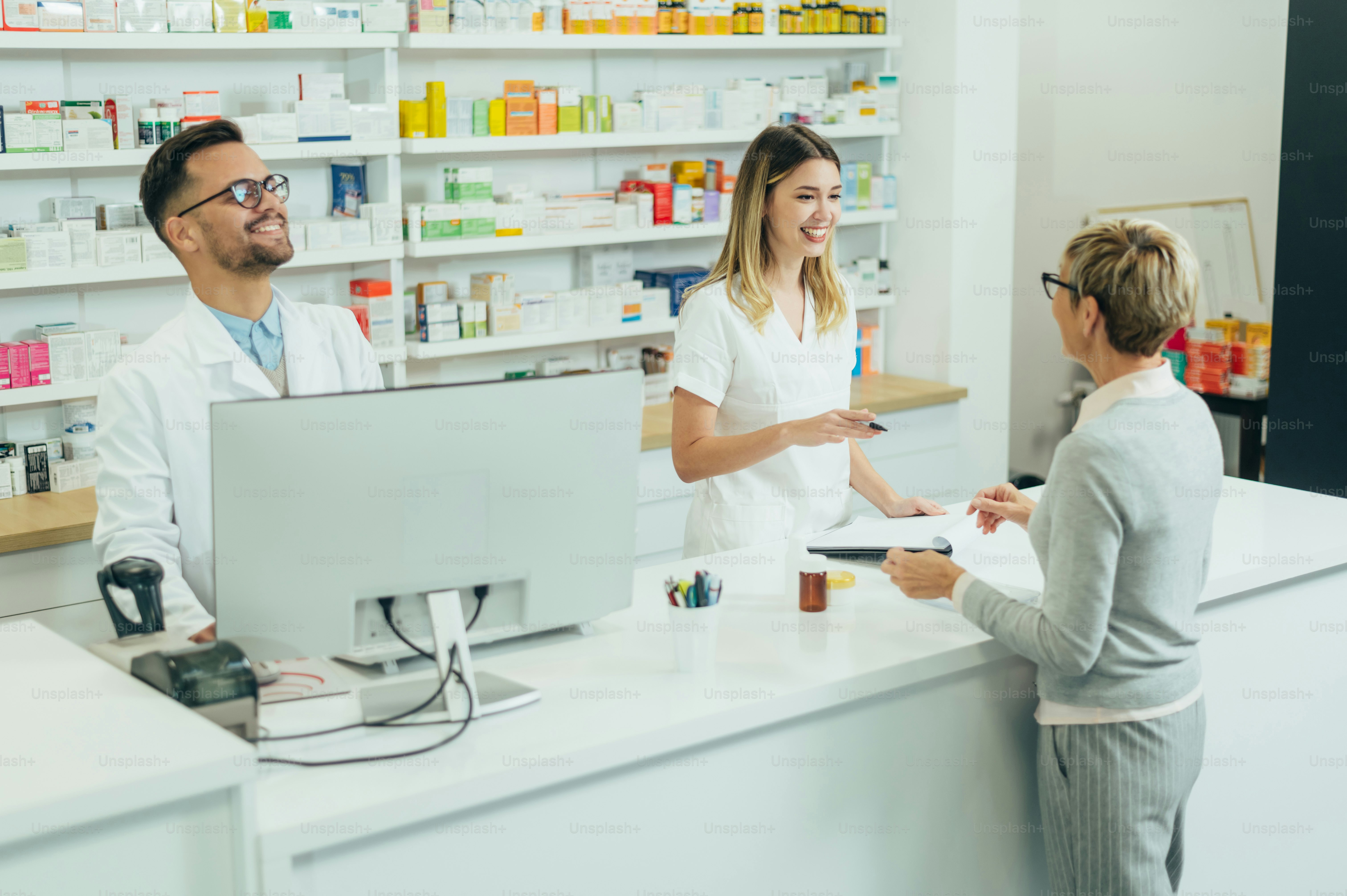 Two pharmacist giving prescription medications to senior female customer in a pharmacy
