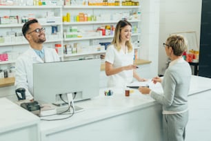 Zwei Apotheker geben verschreibungspflichtige Medikamente an ältere Kundinnen in einer Apotheke