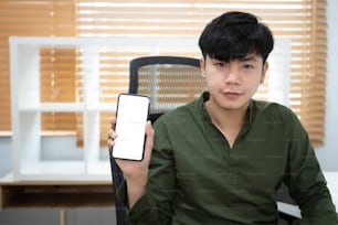 Hübscher junger asiatischer Mann, der ein Smartphone mit leerem Bildschirm hält und zeigt.