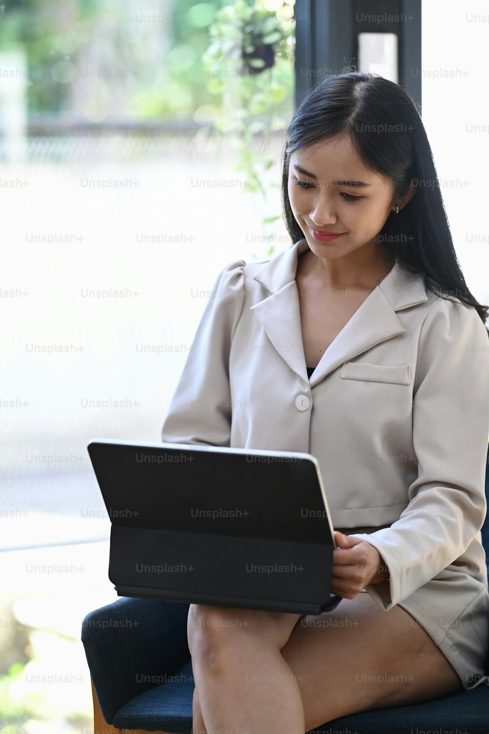 밝은 사무실에 앉아 컴퓨터 태블릿을 사용하는 웃고 있는 젊은 아시아 여성의 초상화.