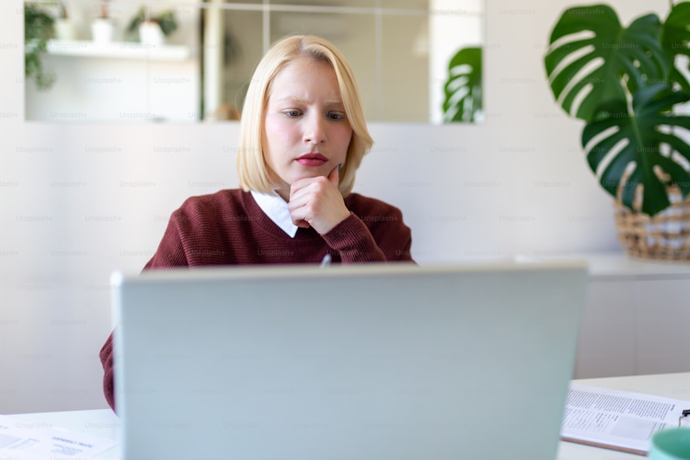 Young woman worker sit at home office reading email or contract feel confused with bad news, frustrated businesswoman stunned by received paperwork correspondence