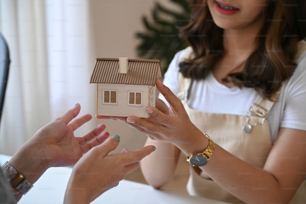 Smiling young woman holding small house model. Real estate investment concept.