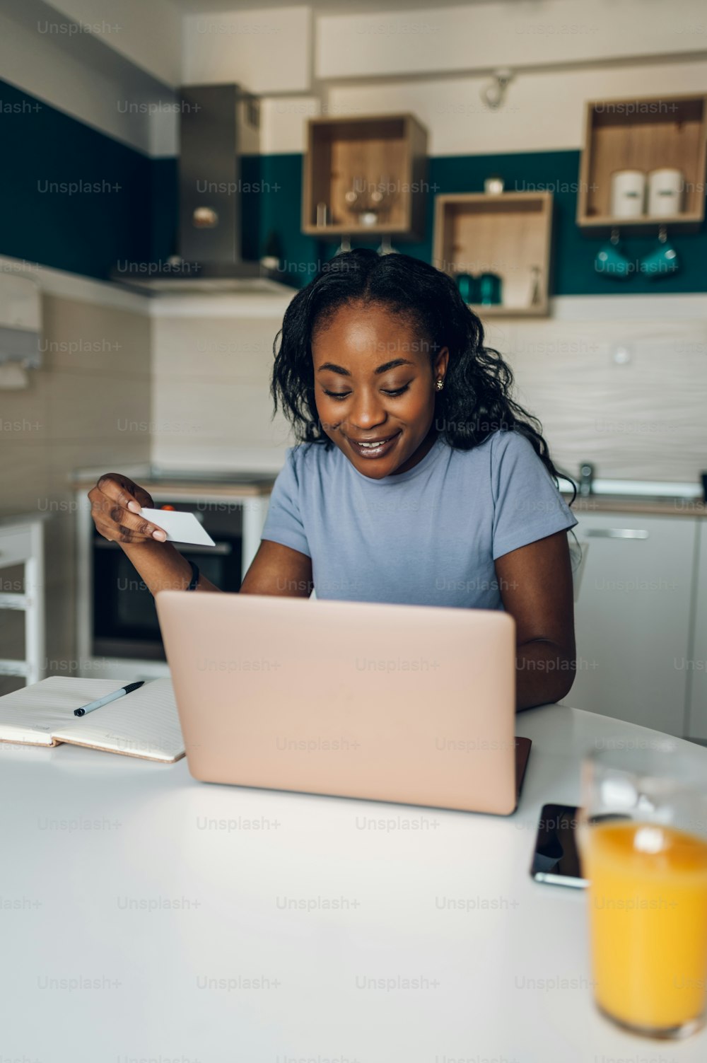아름다운 아프리카계 미국인 여자가 집에서 부엌에서 노트북과 신용 카드를 사용하면서 멀리 쇼핑하고 있다. 판매중인 온라인 구매 비용을 지불합니다.
