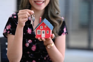 Smiling asian woman holding house model and house key in hand. Real estate investment and insurance concept.