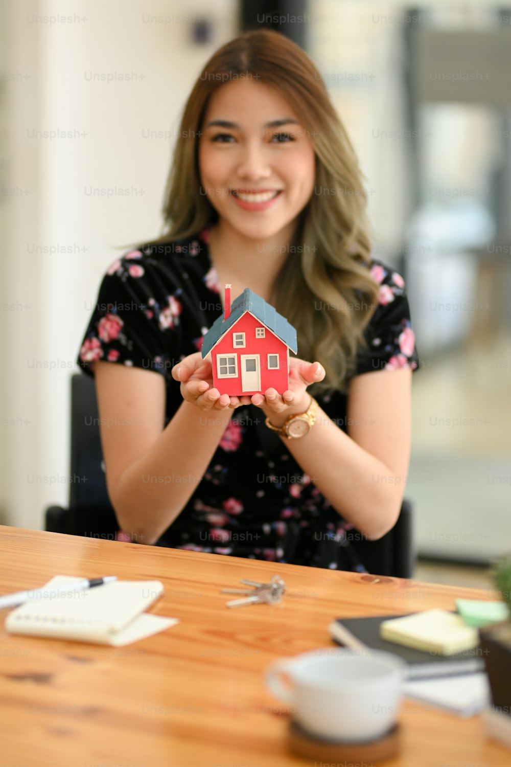 사무실 책상 위에 세련된 집 모델을 들고 있는 아름다운 아시아 여성의 초상화. 주거용 투자, 부동산 구매, 주택 건설.
