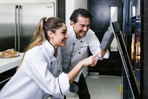 young Latin couple woman and man bakers and baking croissants and bread on oven at kitchen in Mexico Latin America