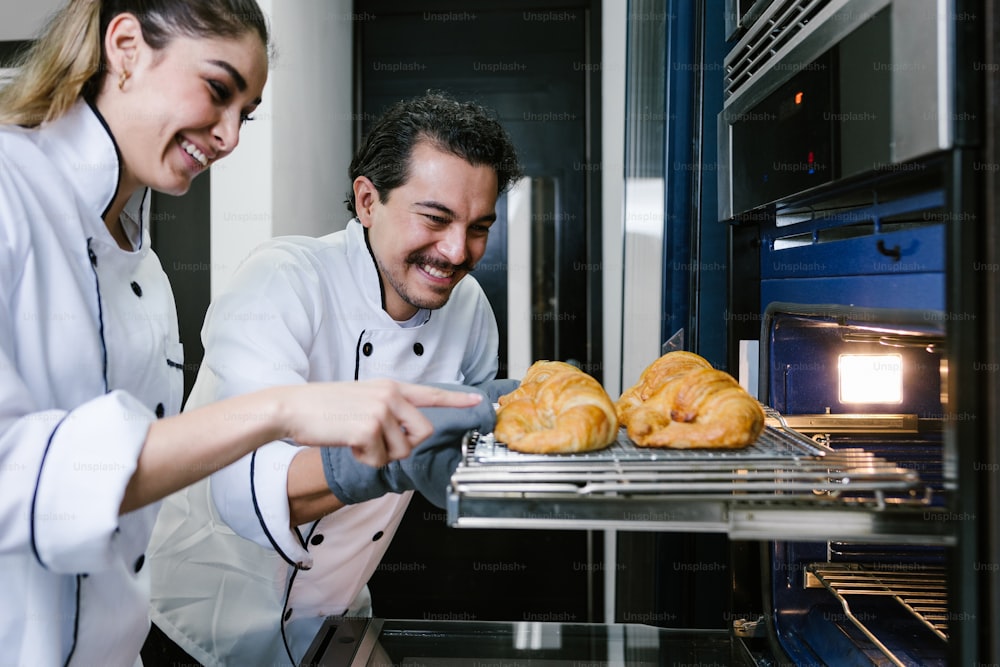young Latin couple woman and man bakers and baking croissants and bread on oven at kitchen in Mexico Latin America