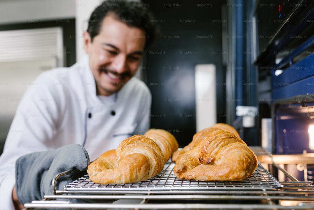 young Latin man baker and baking croissant and bread on oven at kitchen in Mexico Latin America