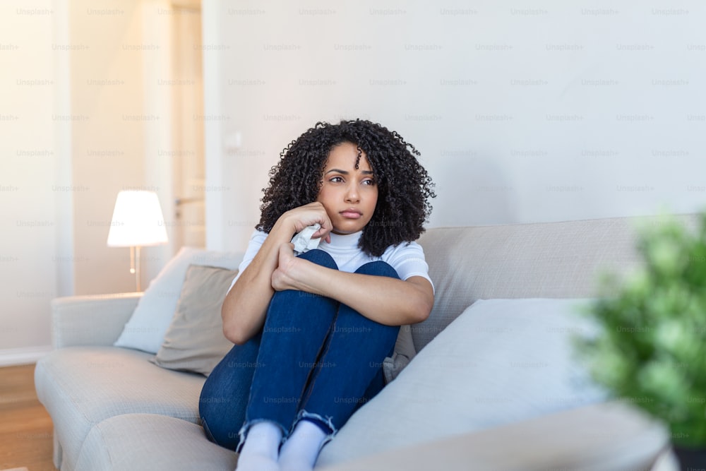 Jovem mulher afro-americana se sentindo chateada, triste, infeliz ou decepcionada chorando solitária em seu quarto. Mulher que sofre de depressão sentada na cama e chorando