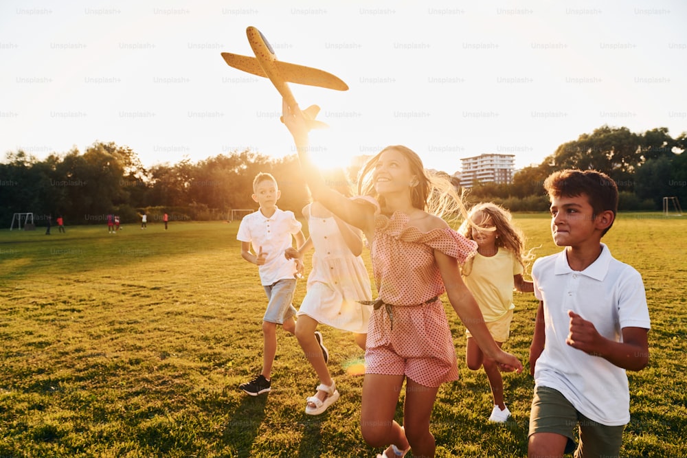 Playing with toy plane. Group of happy kids is outdoors on the sportive field at daytime.