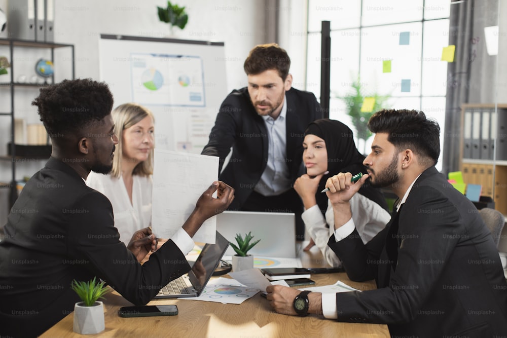 Team of competent financial analysts gathering together at boardroom for brainstorming. Multiracial men and women in formal clothes discussing business plan of common project.