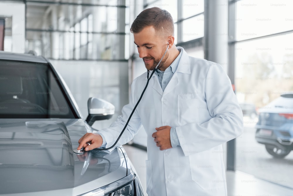 Medic in white coat is using stethoscope on the automobile.
