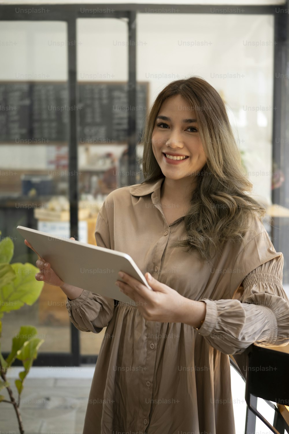 Ritratto di felice proprietario di donna asiatica in piedi nella sua caffetteria e utilizzando la tavoletta digitale.