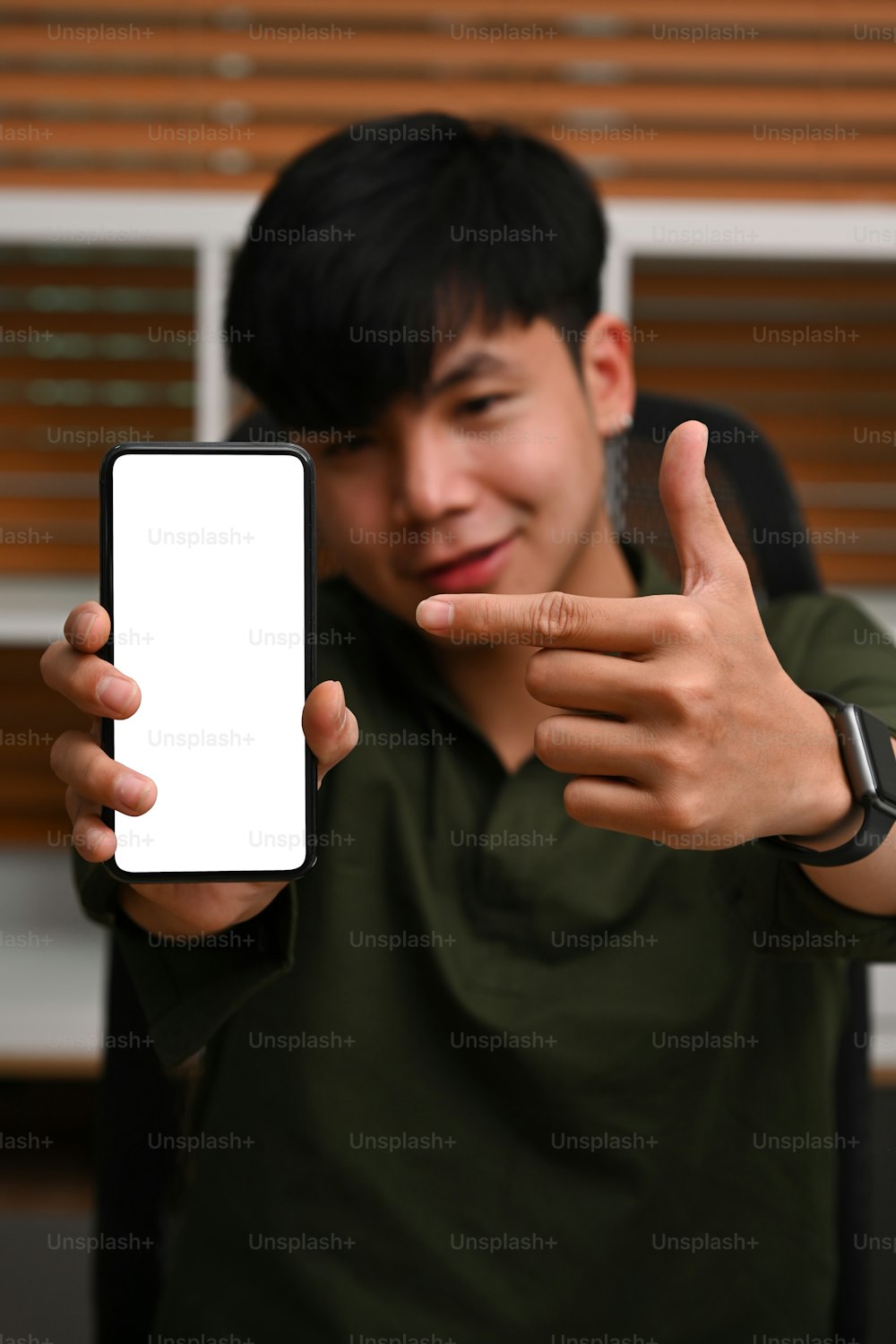 広告用の空白の画面でスマートフォンを見せている若いアジアの男性。
