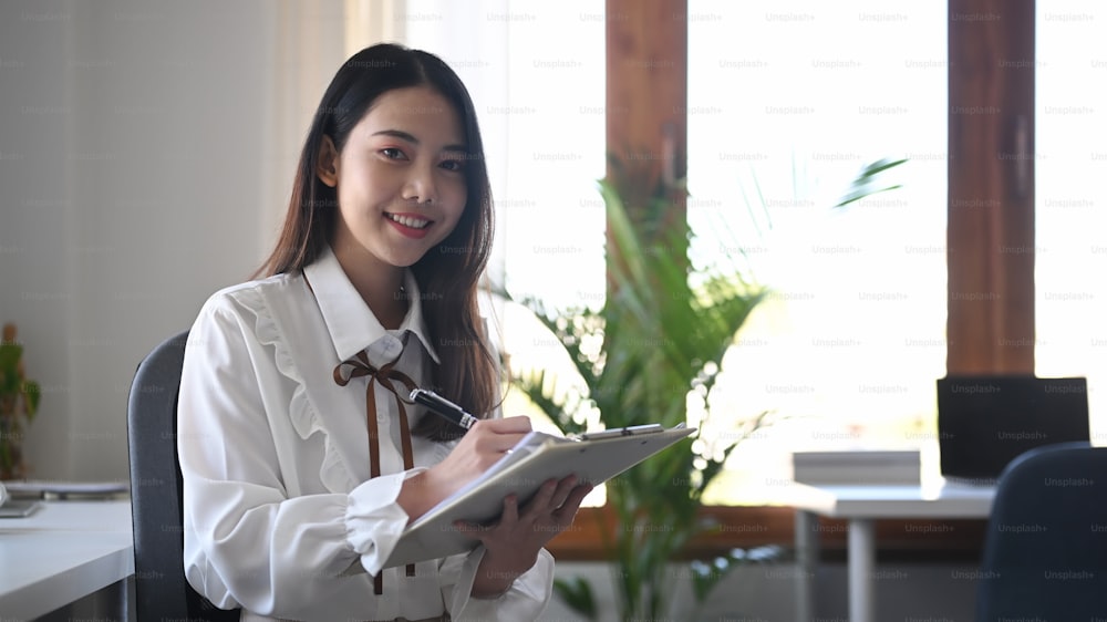Confident business woman holding clipboard and smiling at camera.