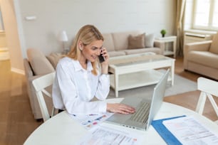 Mulher jovem focada em casa fazendo uma chamada de negócios wile usando laptop. Empreendedor loiro e estiloso trabalhando em casa. Mulher que gerencia contas domésticas e finanças domésticas