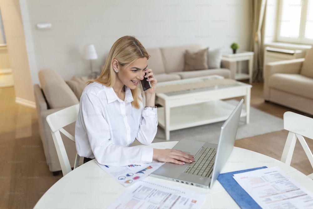 Focused young woman at home making a business call wile using laptop. Blond stylish entrepreneur working at home. Woman managing domestic bills and home finance