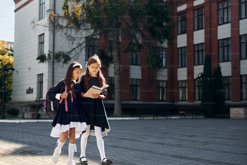 책과 함께. 두 명의 여학생이 학교 건물 근처에서 함께 밖에 있습니다.