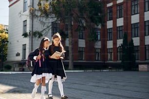 With books. Two schoolgirls is outside together near school building.