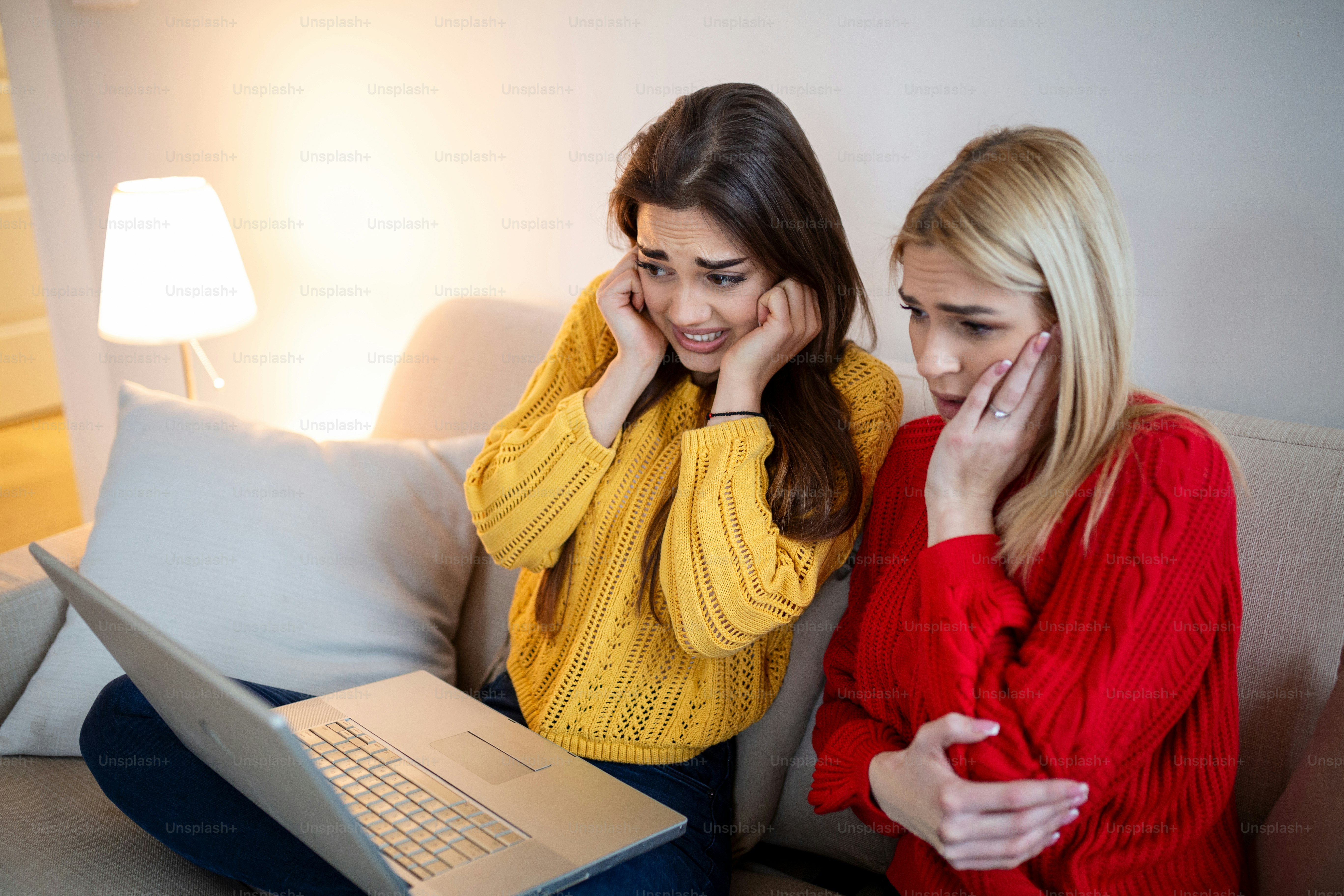 Frightened young women watching movie at home. Girls watching a terror scary movie on tv sitting on a couch at home