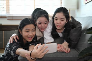 自宅でスマートスマートフォンで自撮りをしている幸せなアジアの女の子。