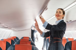 Une jeune hôtesse de l’air vêtue d’une tenue noire formelle se tient à l’intérieur de l’avion.