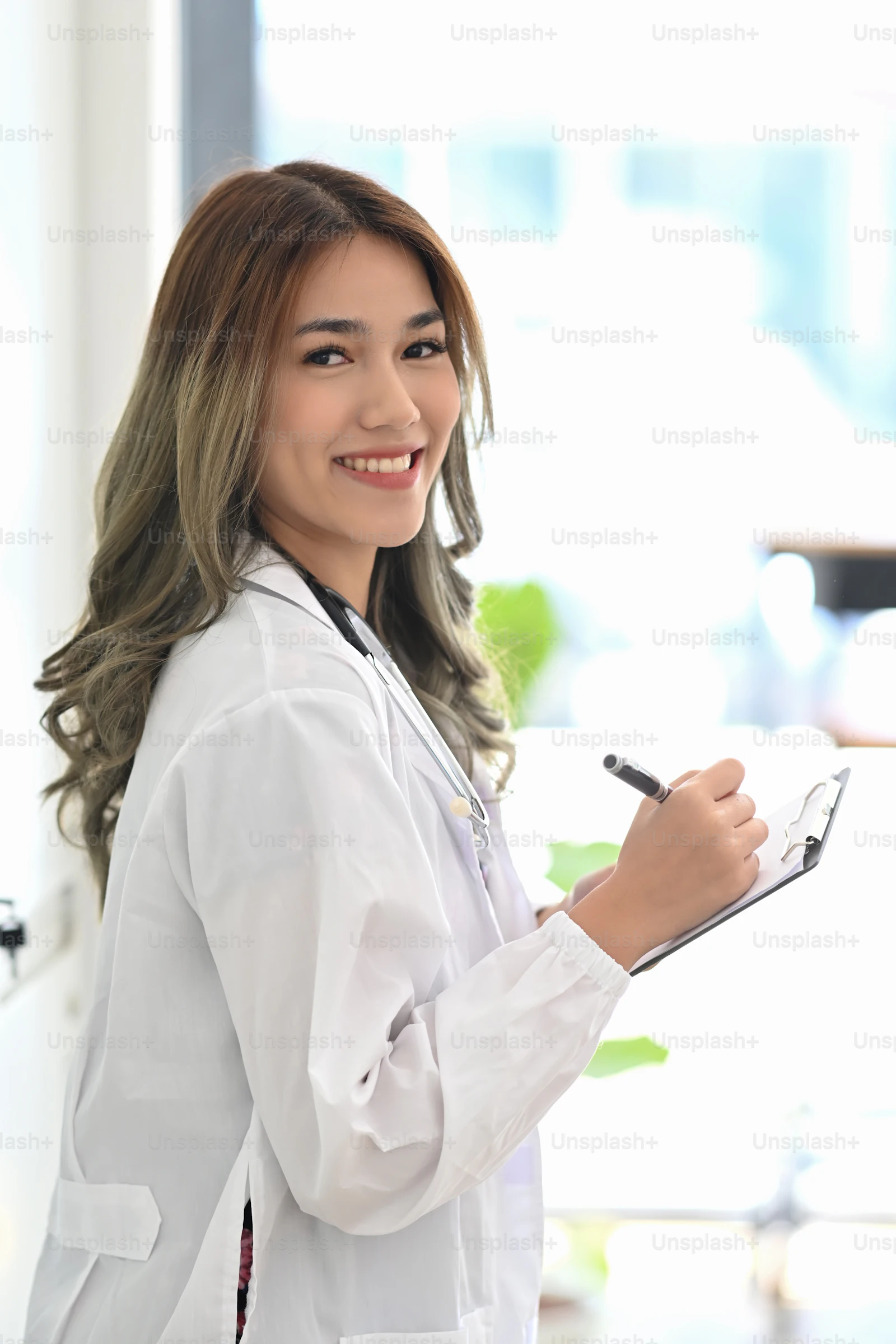 An Asian female doctor in a white coat standing in a bright medical office