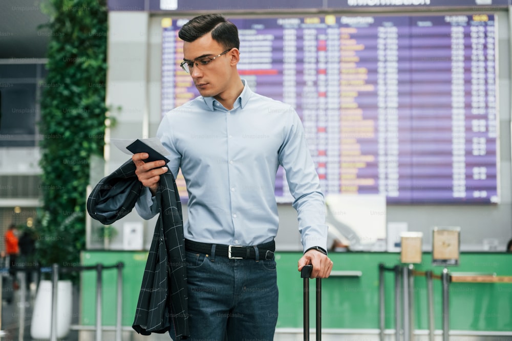 Holding phone. Young businessman in formal clothes is in the airport at daytime.