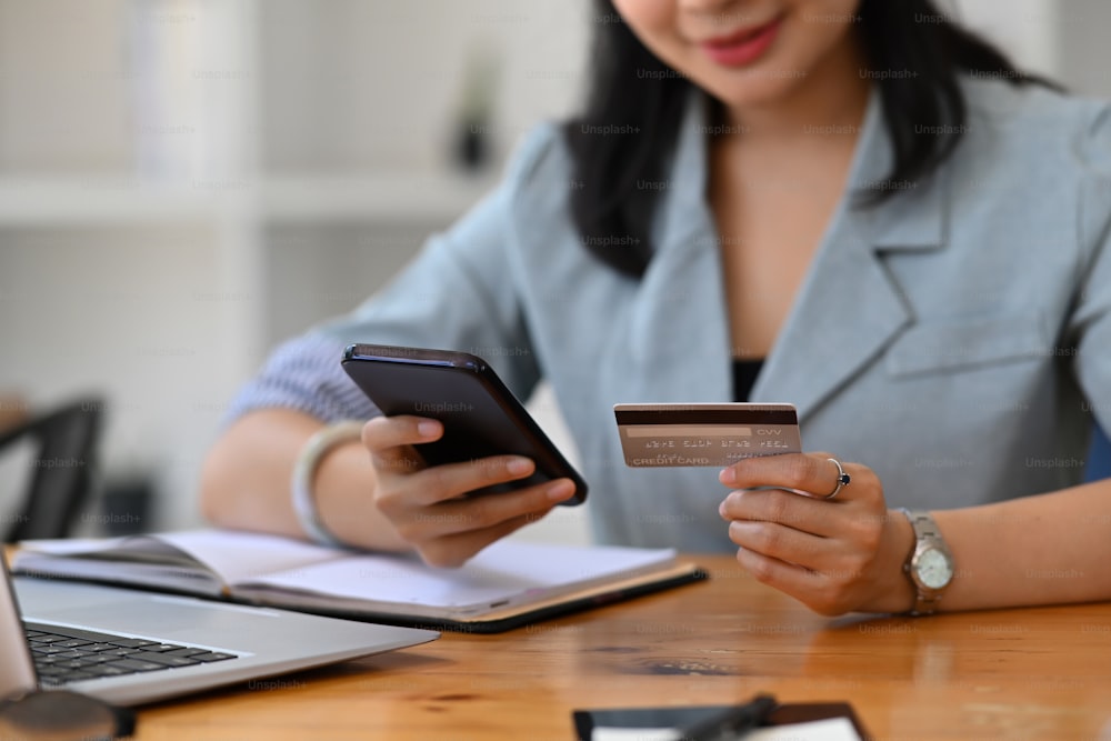 Mulher jovem satisfeita segurando cartão de crédito e usando o telefone inteligente para assar on-line.
