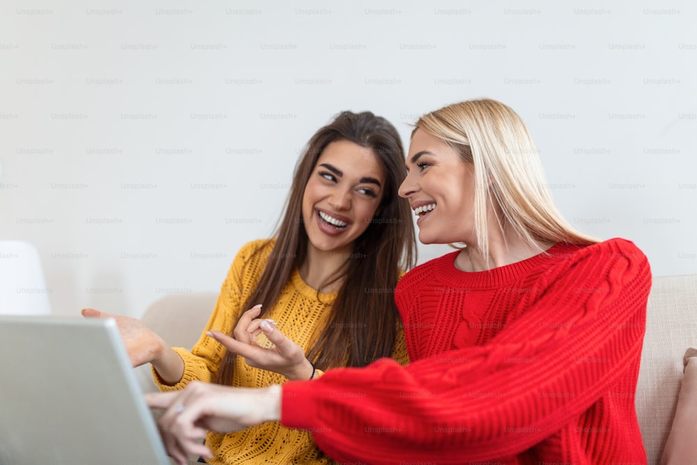 Portrait of a happy girlfriends surfing the net on laptop at home. Lovable blond and brunette girls having fun at home