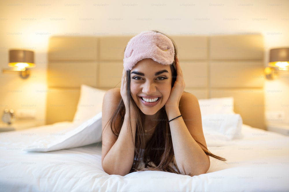 Beautiful girl in bed with sleeping eye mask relaxing. beautiful excited woman in sleeping eye mask lying in bed