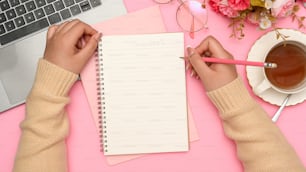 Estudiante universitaria haciendo la tarea, escribiendo un ensayo en su cuaderno escolar en su hermoso escritorio rosa. Vista superior, manecillas de enfoque