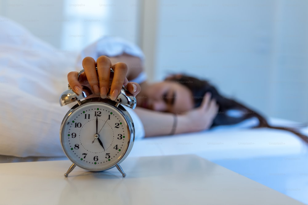 朝5時に目覚まし時計を回すベッドに横たわる女性。手は朝起きる目覚まし時計をオフにし、女の子は電話で朝起きる目見覚まし時計をオフにします。