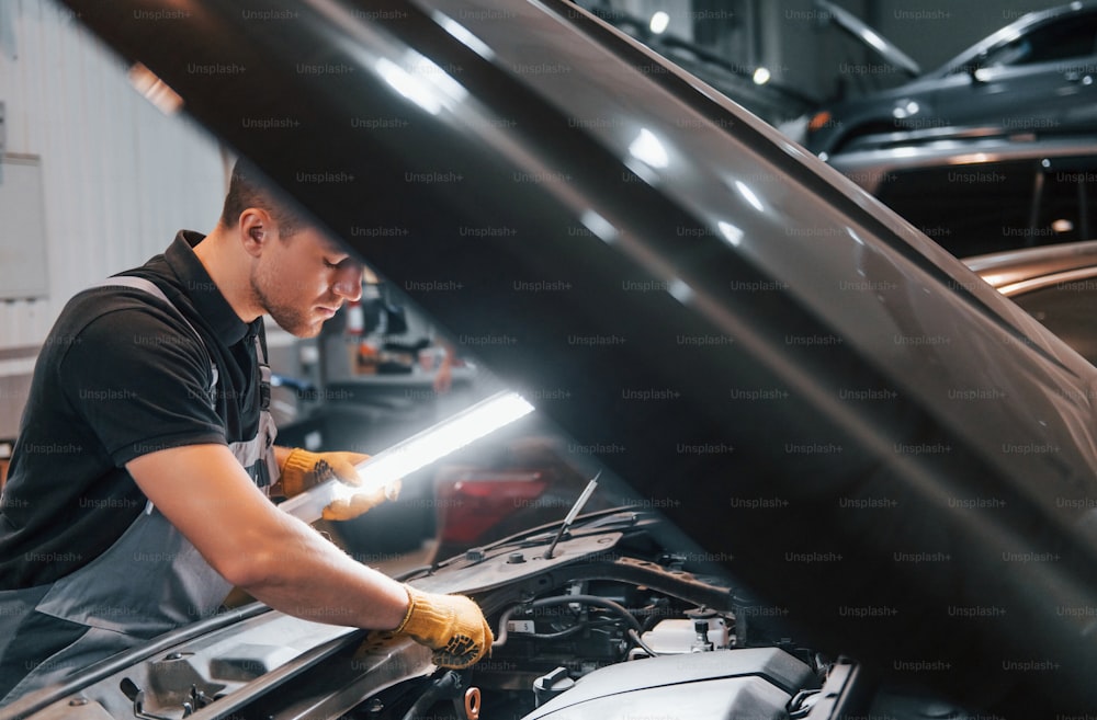 Sotto il cofano. L'uomo in uniforme lavora nel servizio auto.