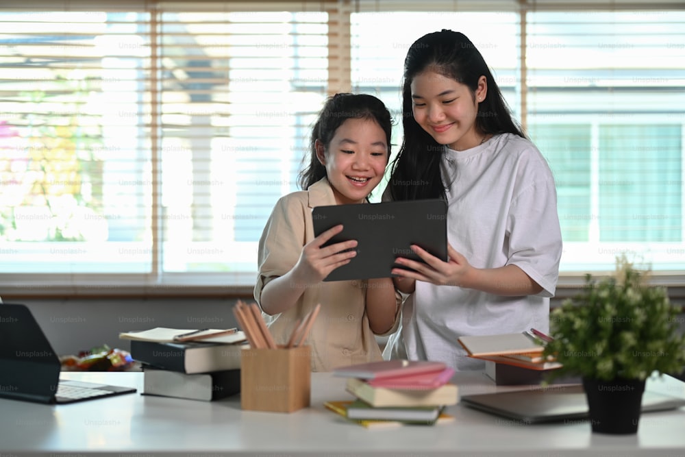 Asian girl using digital tablet with her younger sister in living room.