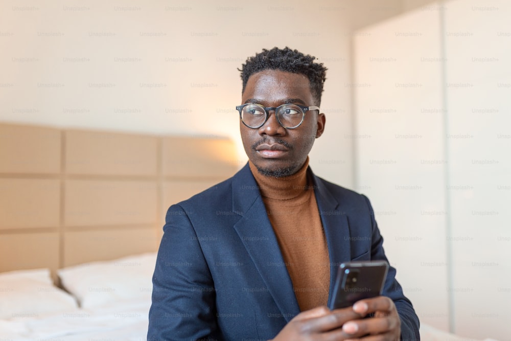 African businessman with smartphone in a hotel room. Handsome man standing at the window, texting. Close up.