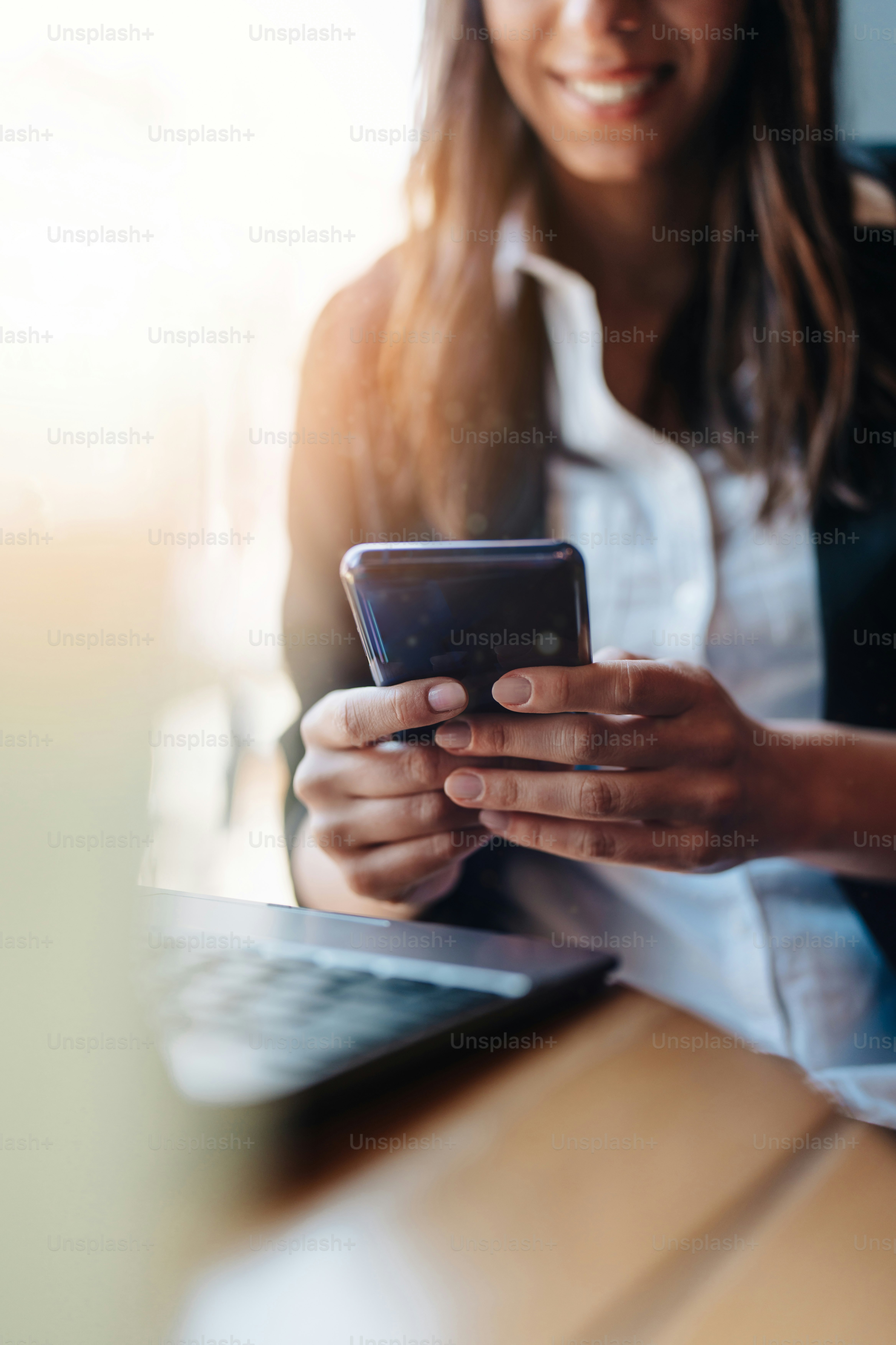 Young business woman or student sitting in cafe bar or restaurant and using smart phone and laptop computer. Close up shot on woman's hand. Beautiful creamy sunlight in background. Selective focus.