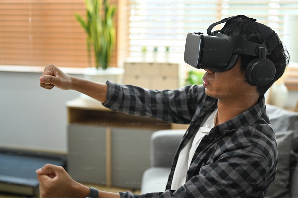Joven asiático alegre jugando a un videojuego de carreras en auriculares de realidad virtual.