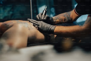 어두운 문신 스튜디오에서 일하는 동안 남자 피부에 문신을 하는 전문 문신 아티스트. 문신. 예술과 디자인의 개념.