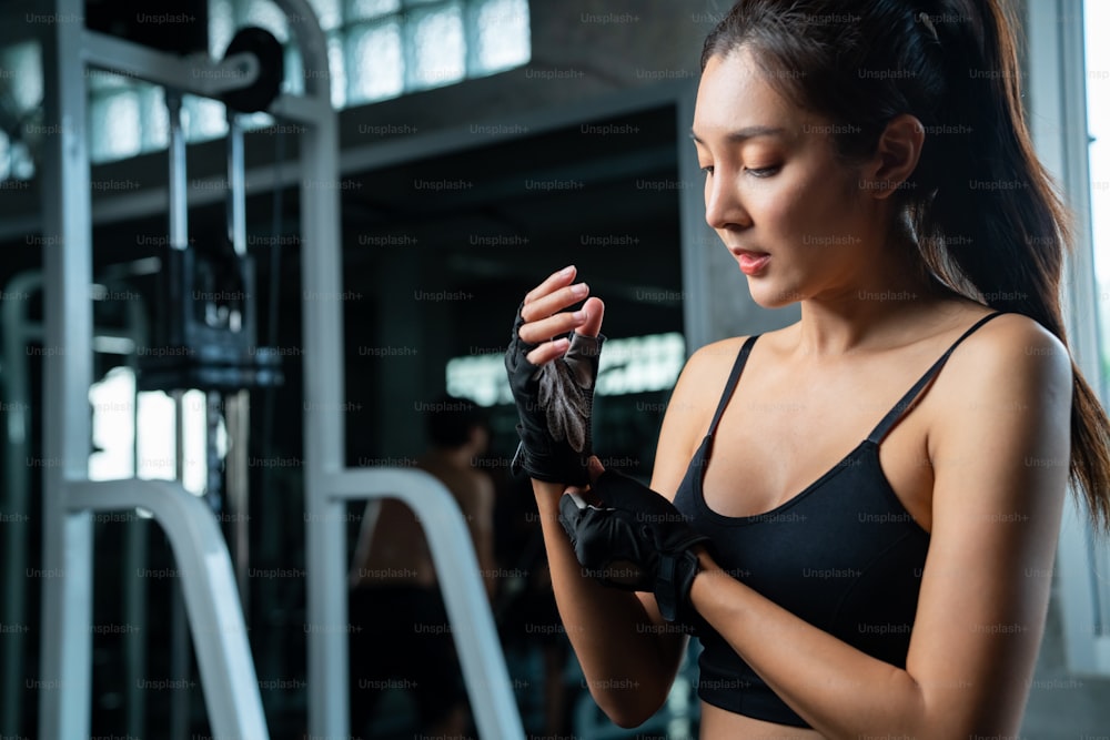 Healthy Asian athletic woman in sportswear wearing sport gloves before workout exercise at fitness gym. Wellness strong female do sport training at sport club. Health care motivation concept