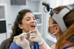 Une patiente ouvre la bouche pour que le médecin regarde dans sa gorge. Femme médecin examinant le mal de gorge d’un patient à la clinique. L’oto-rhino-laryngologiste examine le mal de gorge du patient.