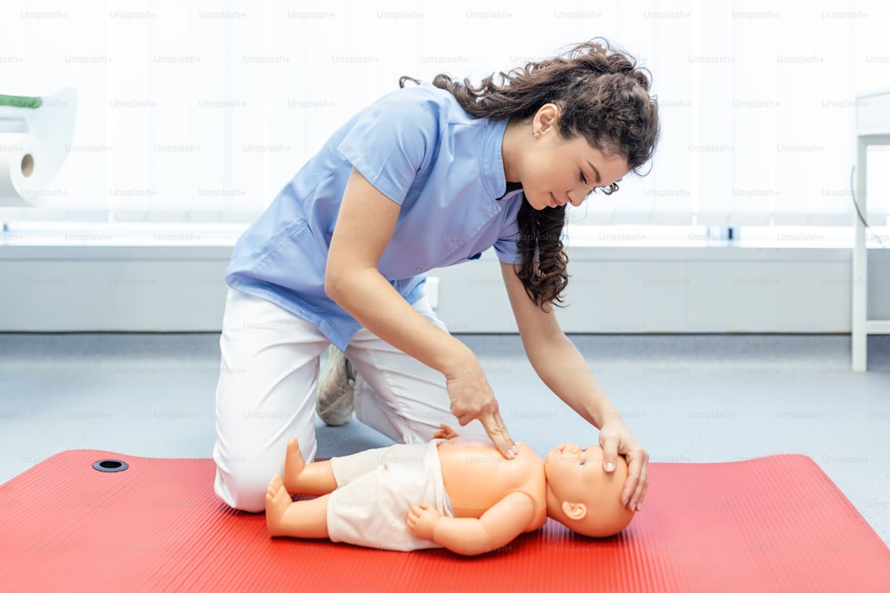 Mujer realizando RCP en una muñeca de entrenamiento de bebé con compresión de una mano. Capacitación en Primeros Auxilios - Reanimación cardiopulmonar. Curso de primeros auxilios sobre maniquí de RCP.