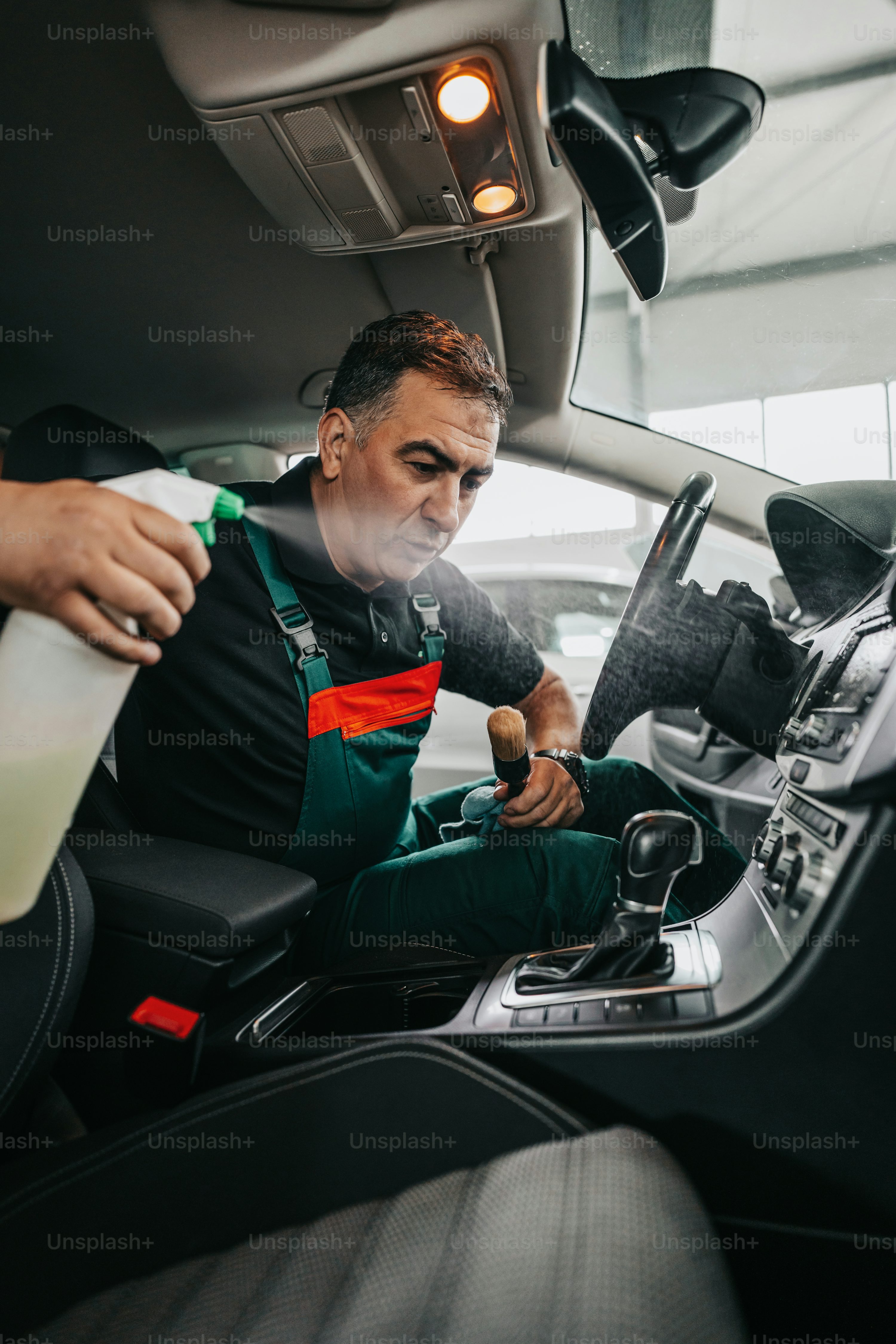Professional worker cleaning car interior and dashboard, car detailing (or valeting) concept. Selective focus. Ultra wide angle shot.