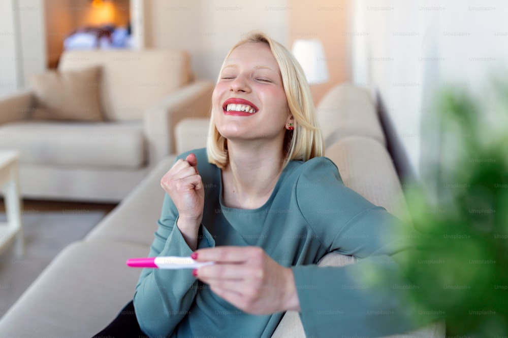 Joven mujer feliz sosteniendo una prueba de embarazo positiva, poca profundidad de campo. Feliz de que vaya a tener un bebé. Finalmente embarazada.