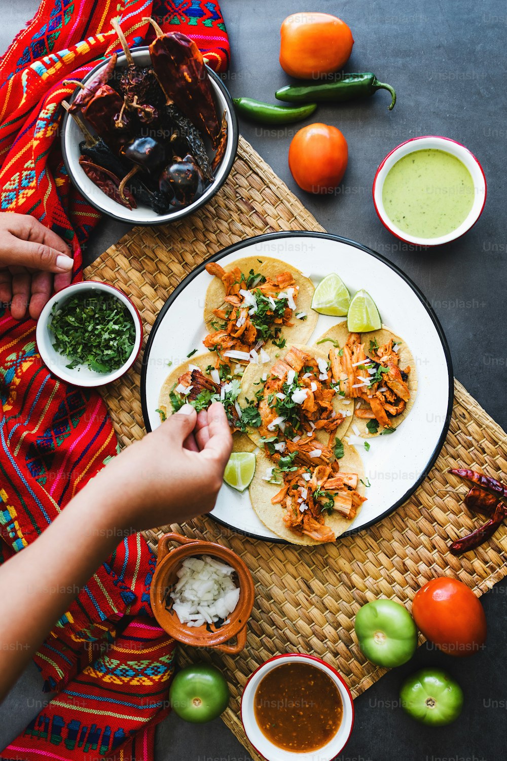 Manos de mujer latina preparando tacos mexicanos con carnitas de cerdo, aguacate, cebolla, cilantro y salsa roja en México