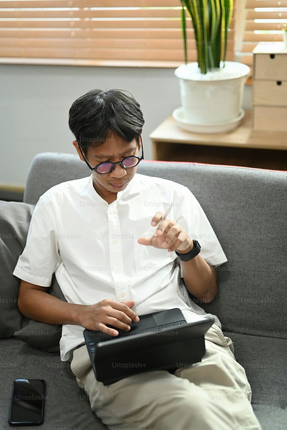 Young man sitting in living room and having a video call with digital tablet.